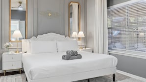 A neatly arranged bedroom with a large bed, two bedside tables, and a window with blinds. - French-Style 5-BD w/ Pool, Playground, Cinema (Lewisville)