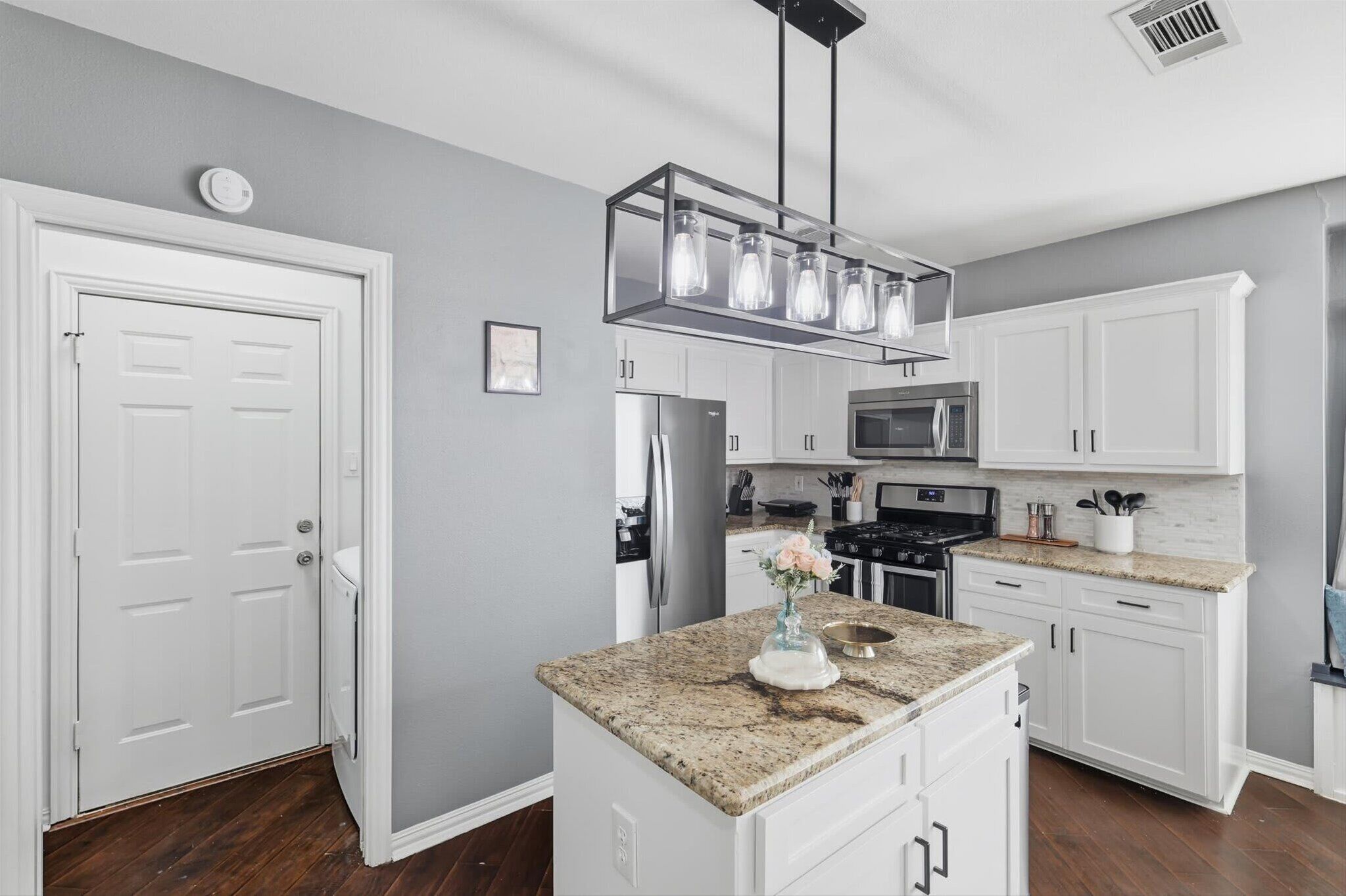 A modern kitchen with white cabinetry, a granite countertop, stainless steel appliances, and a pendant light fixture.