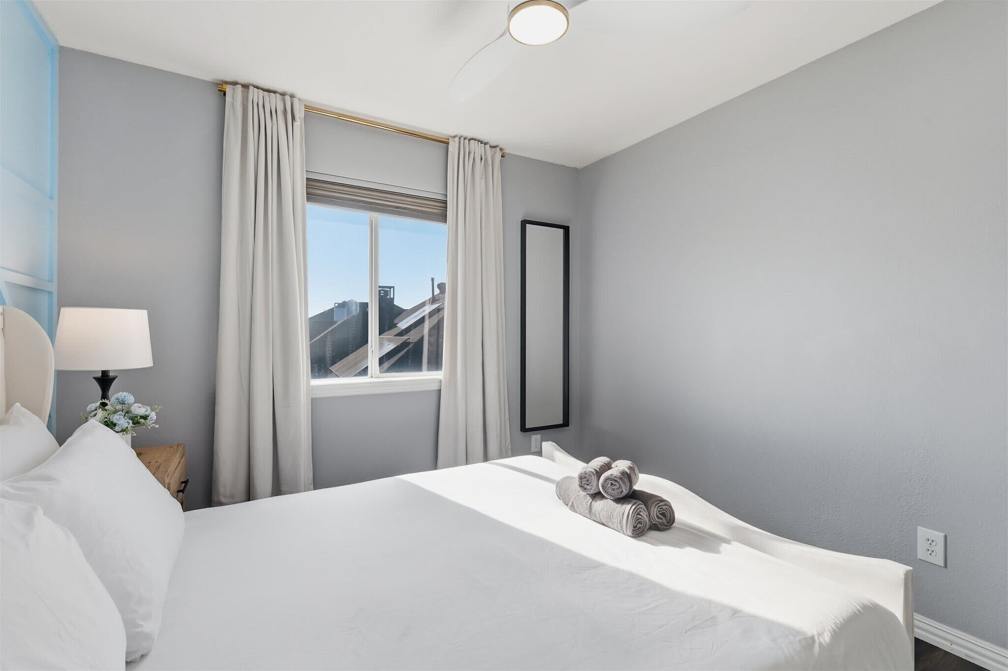 Camera d'albergo con un letto grande, un comodino con una lampada, una finestra con tende e vista sugli edifici.