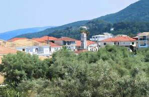 Un pueblo costero con arquitectura tradicional, que incluye una destacada torre del reloj, rodeado de vegetación y colinas.