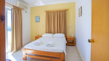 A hotel room with a bed, bedside tables, a wall-mounted air conditioner, a ceiling light, and a door.