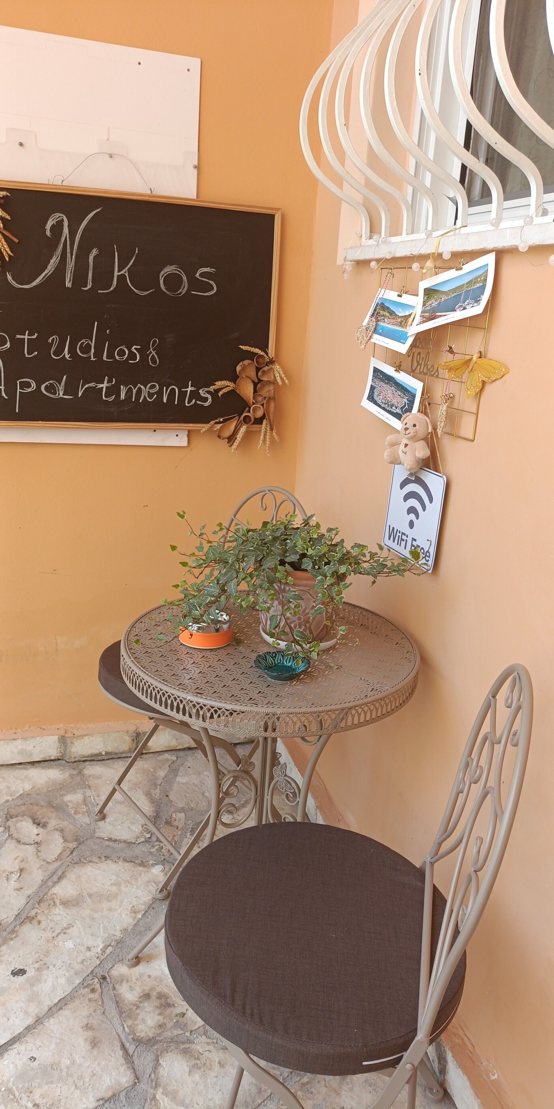 A small round table with a potted plant, a chair, a chalkboard sign, and a wall-mounted photo display.