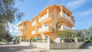 A multi-story residential building with balconies, a stone wall, and a clear sky.