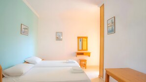 A hotel room with two beds, a wooden nightstand, a small wooden table, a mirror, and two framed pictures on the walls.