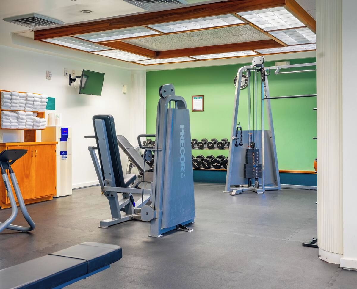 Ein Fitnessstudio mit Kraftgeräten, Hanteln und einer Rezeption mit Handtüchern.