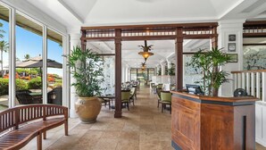 Eine großzügige Lobby mit einem Holzbüro, großen Topfpflanzen und Blick auf den Garten.