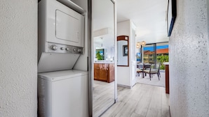 A laundry room with a washing machine and dryer, a wooden cabinet, and a glass door leading to a balcony with outdoor seating. - Papakea Ocean View Resort Condo | Sleeps 7, Pools, Hot Tubs, Tennis, Lanai, AC (Lahaina)