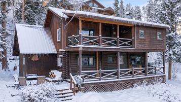 Une cabane en rondins à deux étages, dotée d’un balcon et entourée d’arbres couverts de neige.