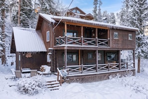 A two-story log cabin with a balcony, surrounded by snow-covered trees. - Cabin at Timber Run Rustic cabin, mt views, 3 bedrooms and open floor plan (Winter Park)