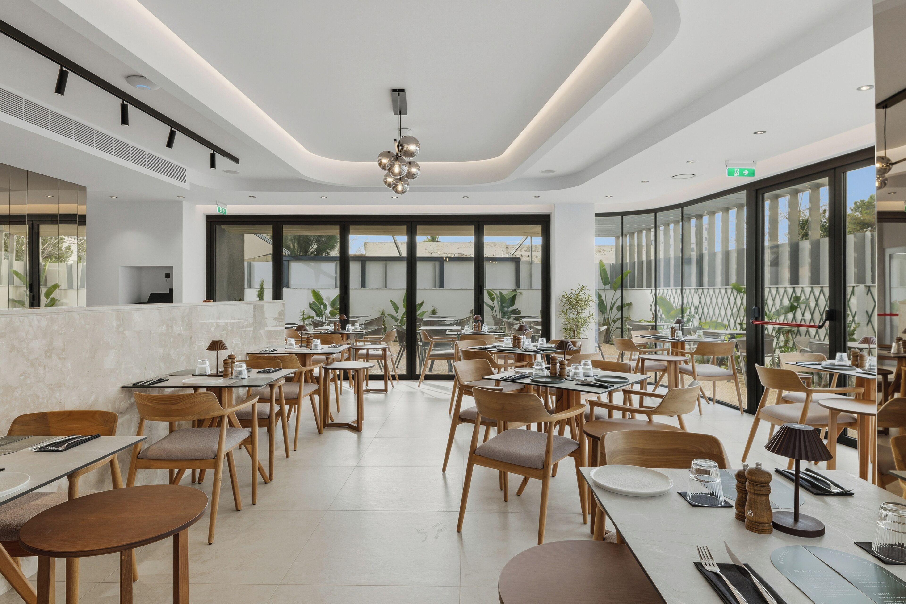 A spacious restaurant with high ceilings, modern lighting, and large windows offering a view of the outdoors.