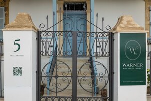 Entrada de un hotel con una reja de hierro forjado, una puerta azul y un letrero que dice Warner Boutique Hotel.