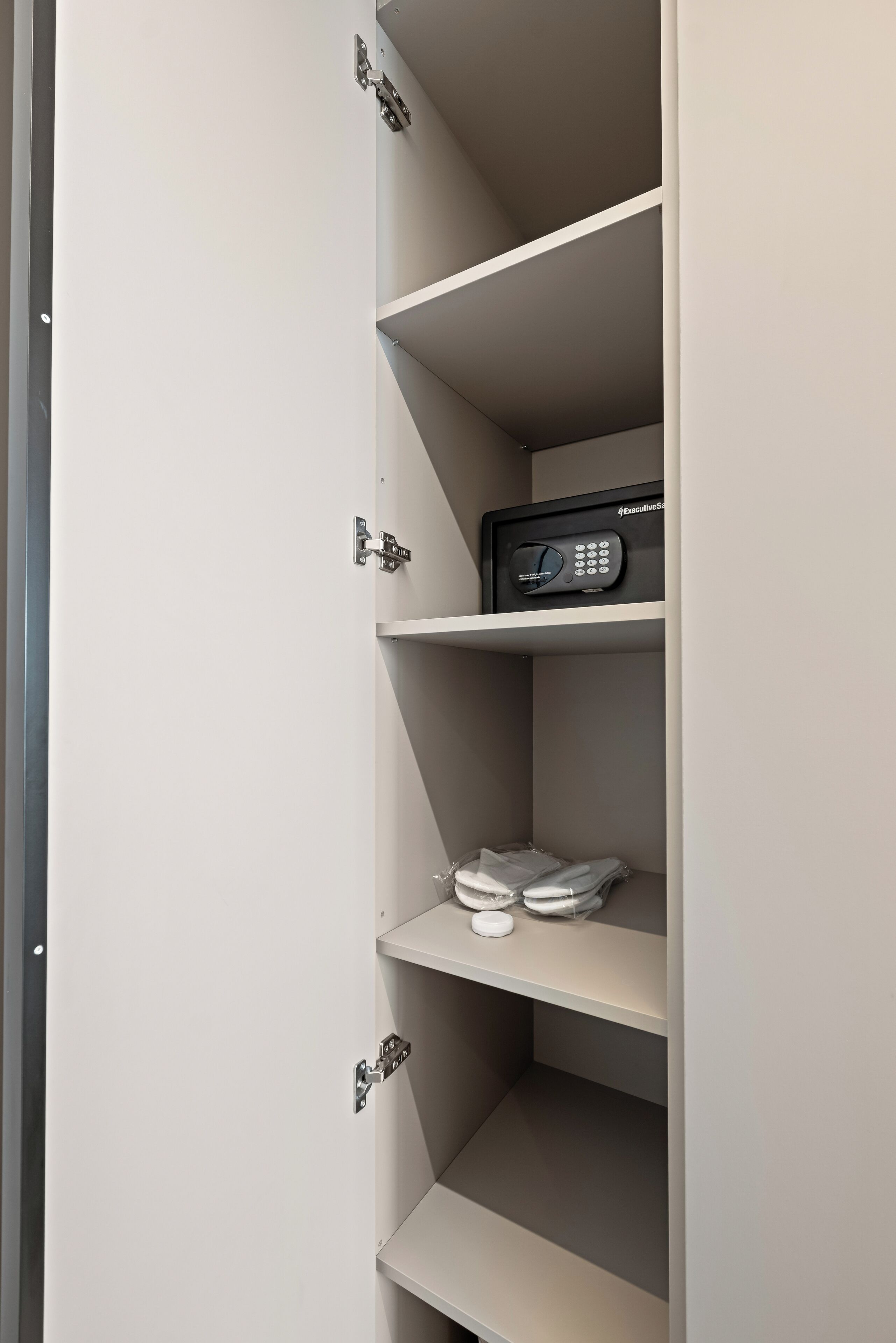 A closed cabinet with multiple shelves, including a microwave on the top shelf and a pair of shoes on the bottom shelf.