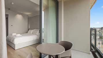 Une chambre moderne avec un grand lit, une porte vitrée donnant sur un balcon et une table ronde avec des chaises.