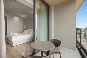 Un dormitorio moderno con una cama grande, un ventanal de vidrio que da a un balcón y una mesa redonda con sillas.