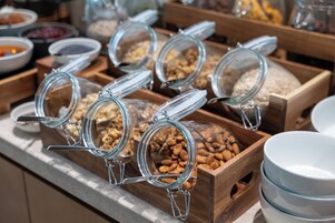 Un bufé con diversos alimentos en recipientes de vidrio y bandejas de madera.