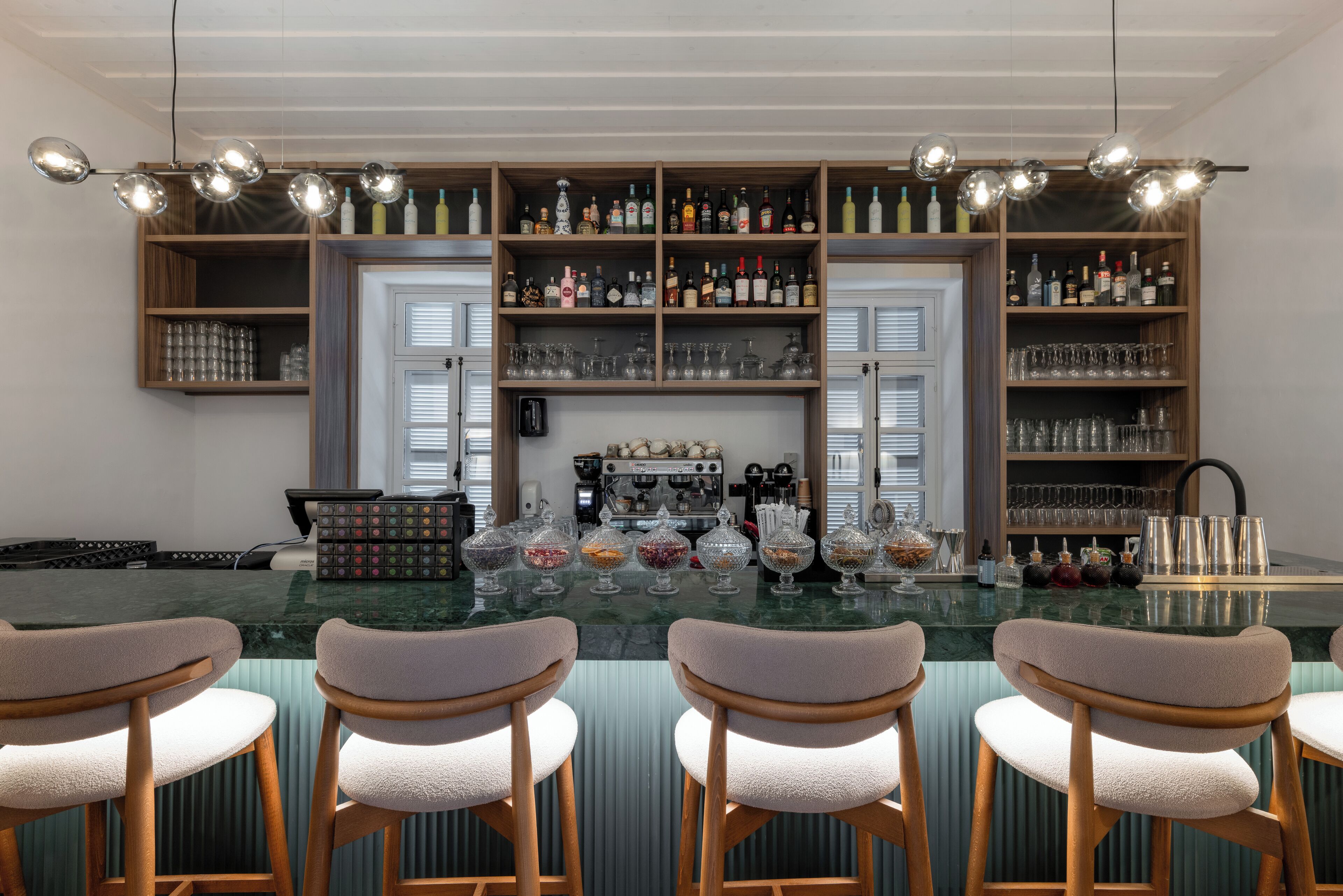 Zona de bar con encimera de mármol, taburetes y estanterías llenas de botellas y vasos.