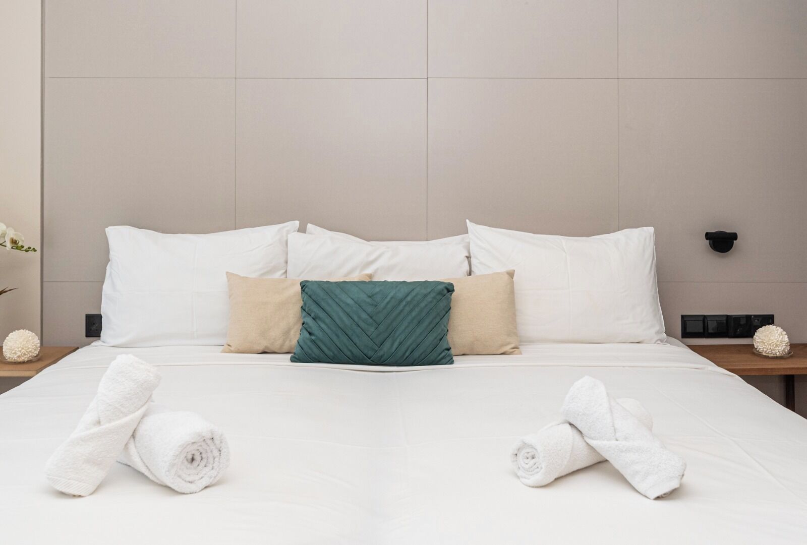 A neatly made bed with white linens, a green pillow, and two beige pillows.