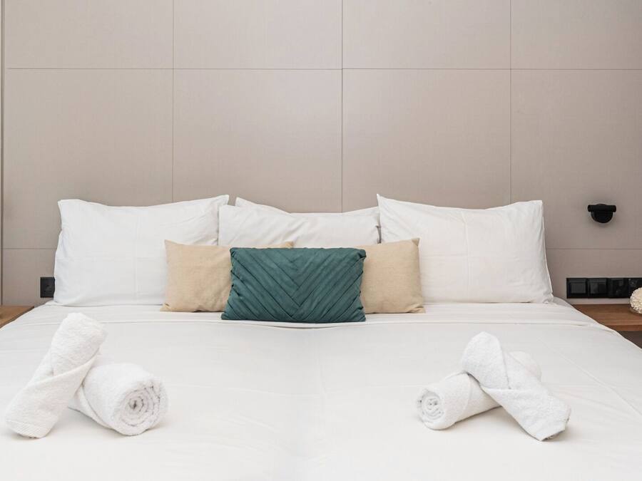 A neatly made bed with white linens, a green pillow, and two beige pillows.