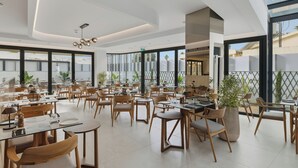 A spacious restaurant with high ceilings, large windows, and modern wooden furniture. - Warner Boutique Hotel (Larnaca)