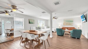 Ein geräumiger Wohnbereich mit einem Holzesstisch, weißen Stühlen, einer Couch und blaugrünen Sessel.