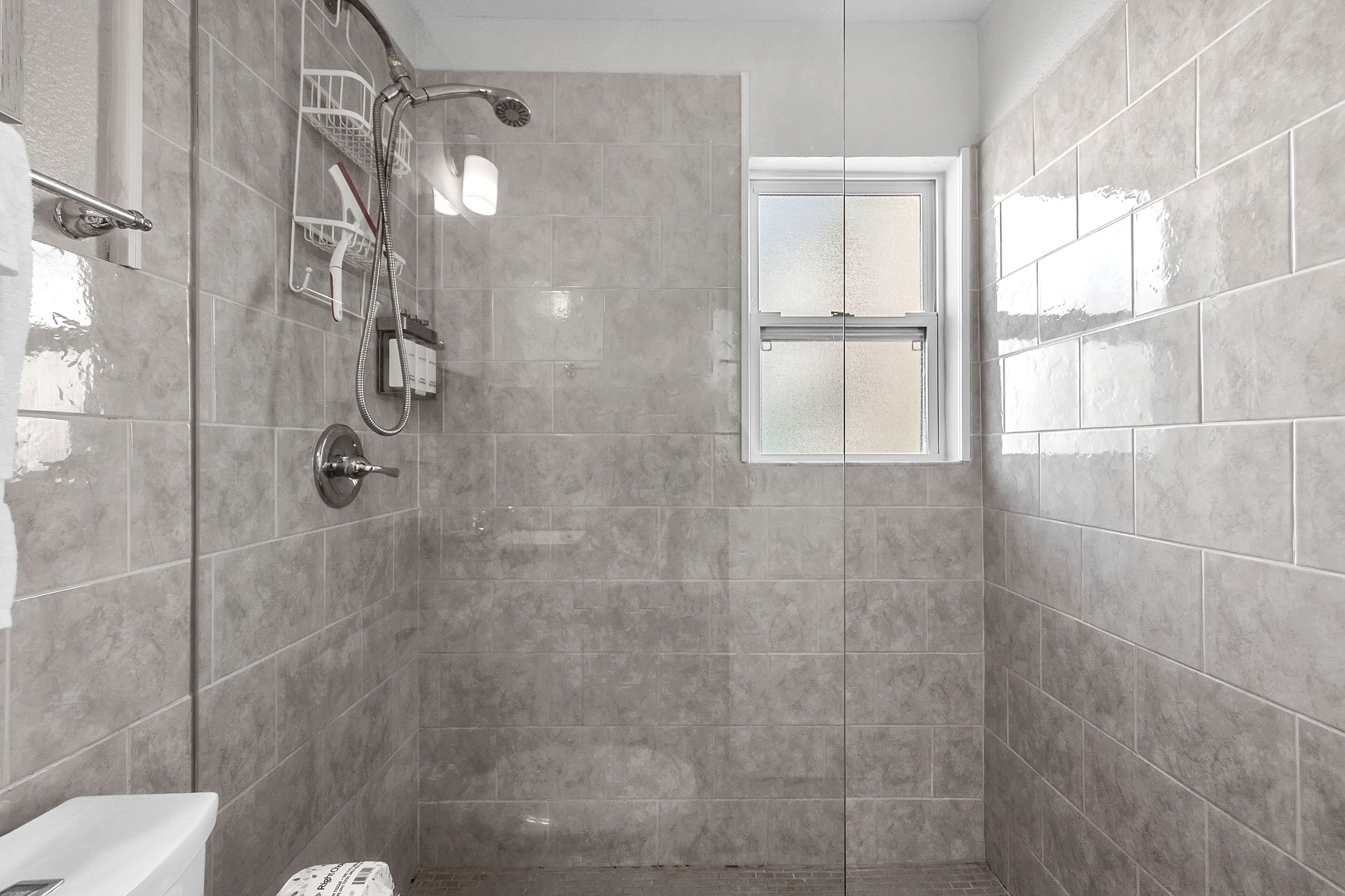 A bathroom with a shower, a toilet, and a window.