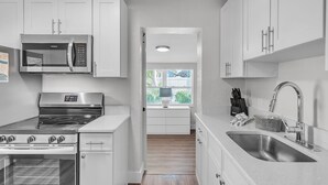 Una cocina moderna con armarios blancos, electrodomésticos de acero inoxidable y un amplio ventanal que proporciona luz natural.
