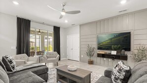 A modern living room with grey sofas, a coffee table, and a flat-screen TV mounted on the wall. - Family Fun Villa w Pool, Hot Tub & Game Room (Davenport)