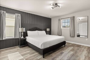 Une chambre à coucher avec un grand lit, deux tables de chevet avec des lampes, un miroir et une fenêtre avec des rideaux.