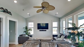 Ein großzügiges Wohnzimmer mit einer großen Ledersofa, einem Deckenventilator, einem Flachbildfernseher und großen Fenstern.