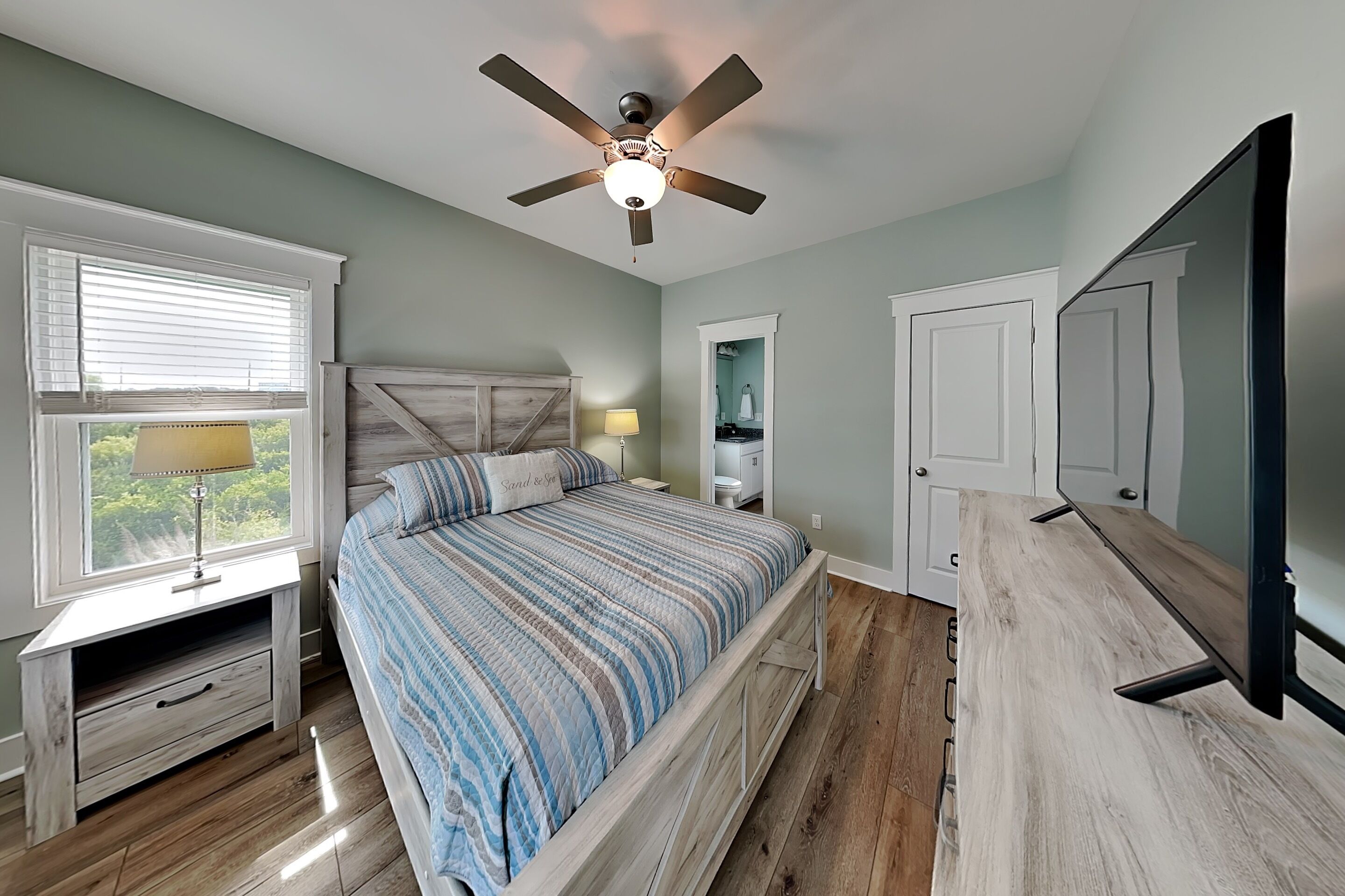 Une chambre à coucher comprenant un lit, un ventilateur de plafond, une table de chevet, une lampe, une commode et un téléviseur.