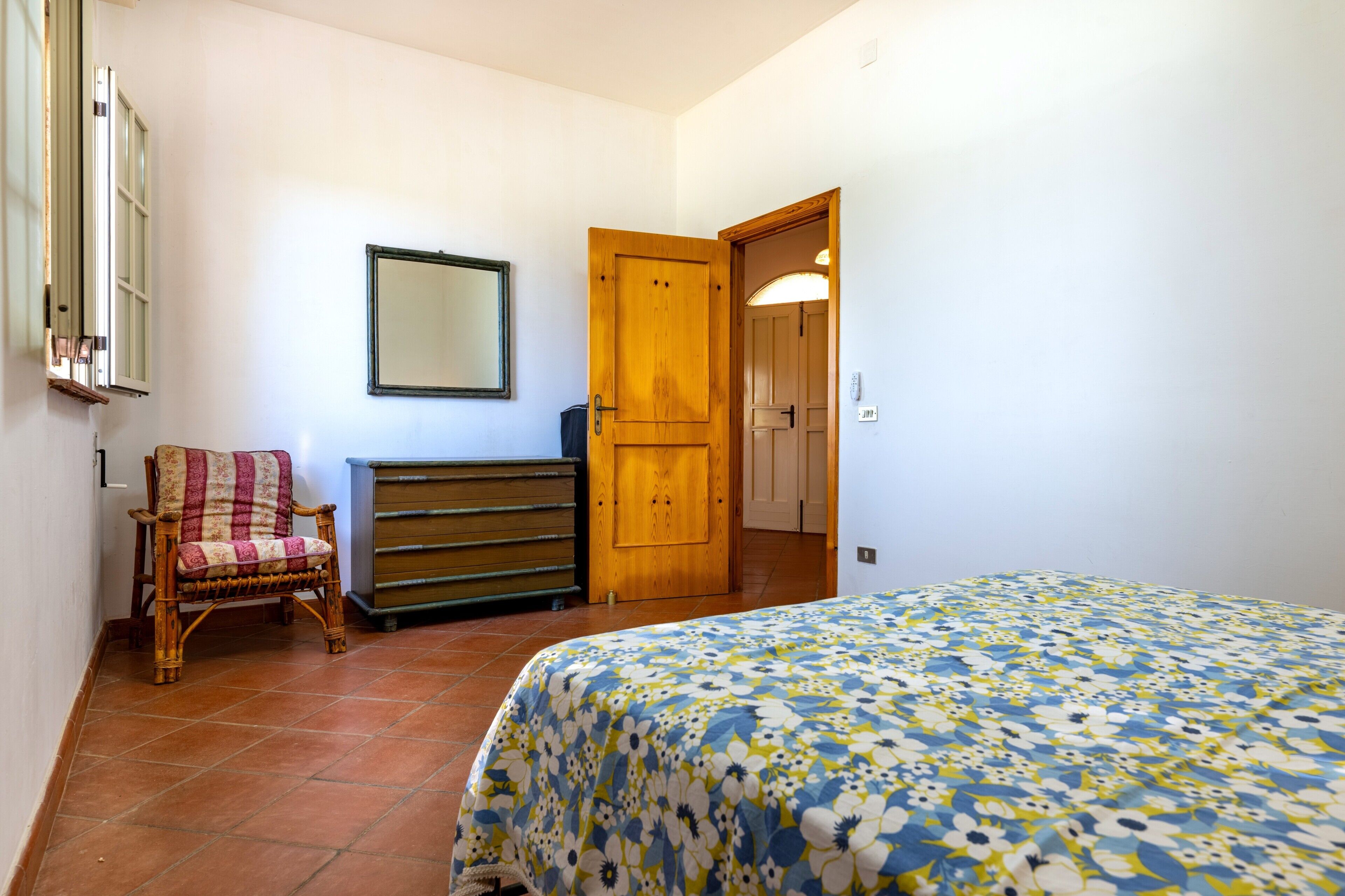 A bedroom with a bed, a wooden door, a chair, a dresser, and a mirror on the wall.