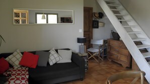 Un salon comprenant un canapé, un fauteuil, une commode en bois, un miroir et un escalier.