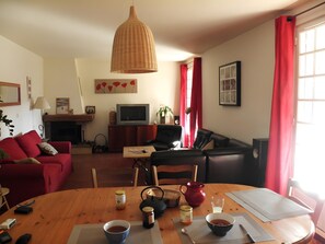 Un salon avec un canapé, un téléviseur, une cheminée, une table à manger avec de la nourriture et des boissons, et une fenêtre avec des rideaux rouges.