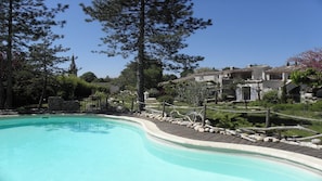 Une piscine dotée d’une terrasse en bois, entourée d’arbres et d’un mur de pierre.