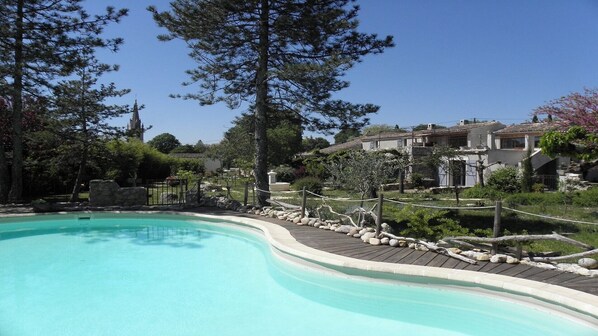 A swimming pool with a wooden deck, surrounded by trees and a stone wall.