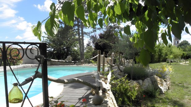 Une piscine dotée d’une terrasse en bois, entourée de rochers et de verdure.