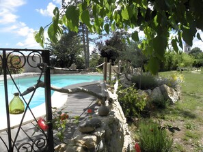 A pool with a wooden deck, surrounded by rocks and greenery.