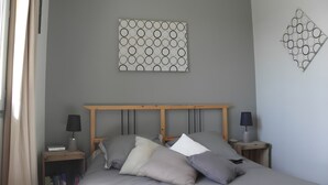 Une chambre à coucher comprenant un lit, deux tables de chevet, une œuvre d’art accrochée au mur et une fenêtre avec des rideaux.