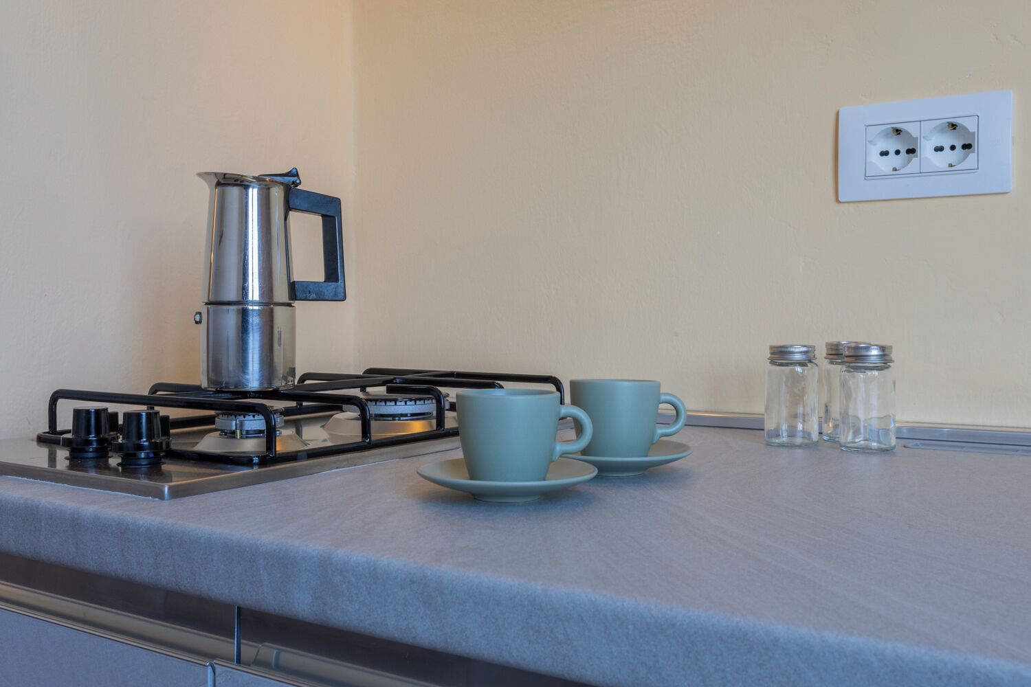 A kitchen with a gas stove, a kettle, two cups, and salt and pepper shakers on the counter.