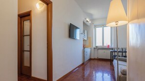 A hallway with wooden flooring leading to a kitchen area with a window, a dining table, and a TV mounted on the wall. - Casa Cecchi by Wonderful Italy (Turin)