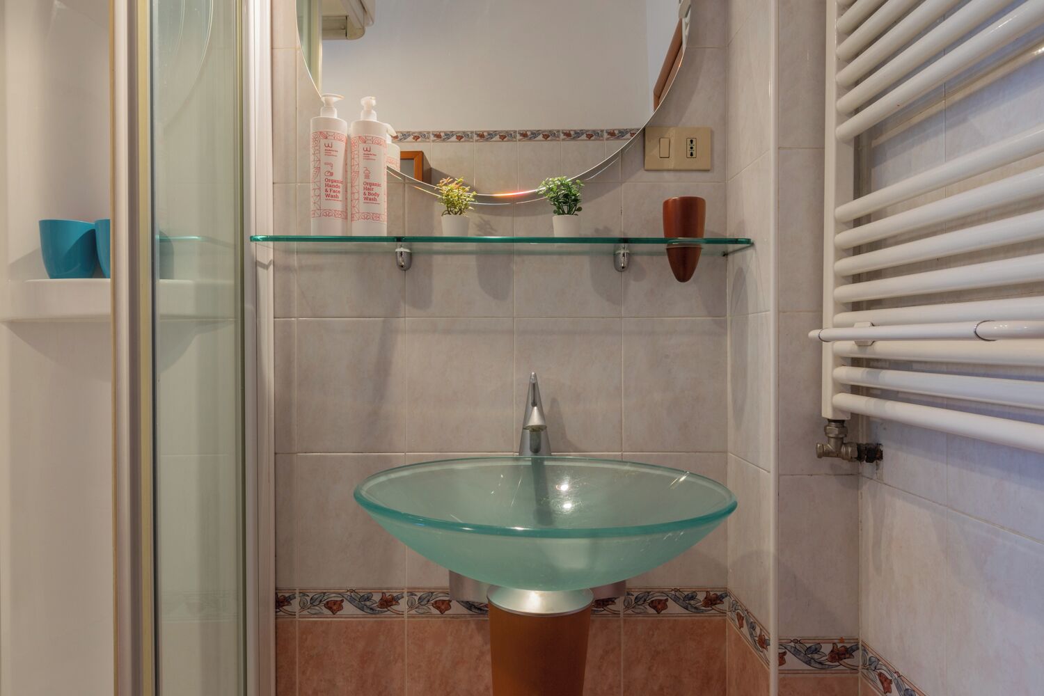 Une salle de bain avec un lavabo en verre, un miroir et un porte-serviettes.