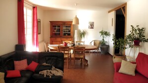 A living room with a black leather sofa, a red sofa, a dining table with chairs, a cabinet, and potted plants. - Les Berbéris – Gîte in Southern Ardèche (Chandolas)