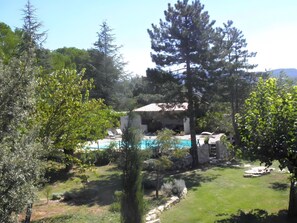 Un espace piscine avec un bâtiment en arrière-plan, le tout entouré d’arbres.