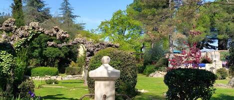 A garden with a fountain, surrounded by greenery and trees.