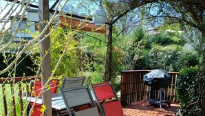 Un terrazzo in legno con tavolo e sedie, circondato da vegetazione e da una recinzione.