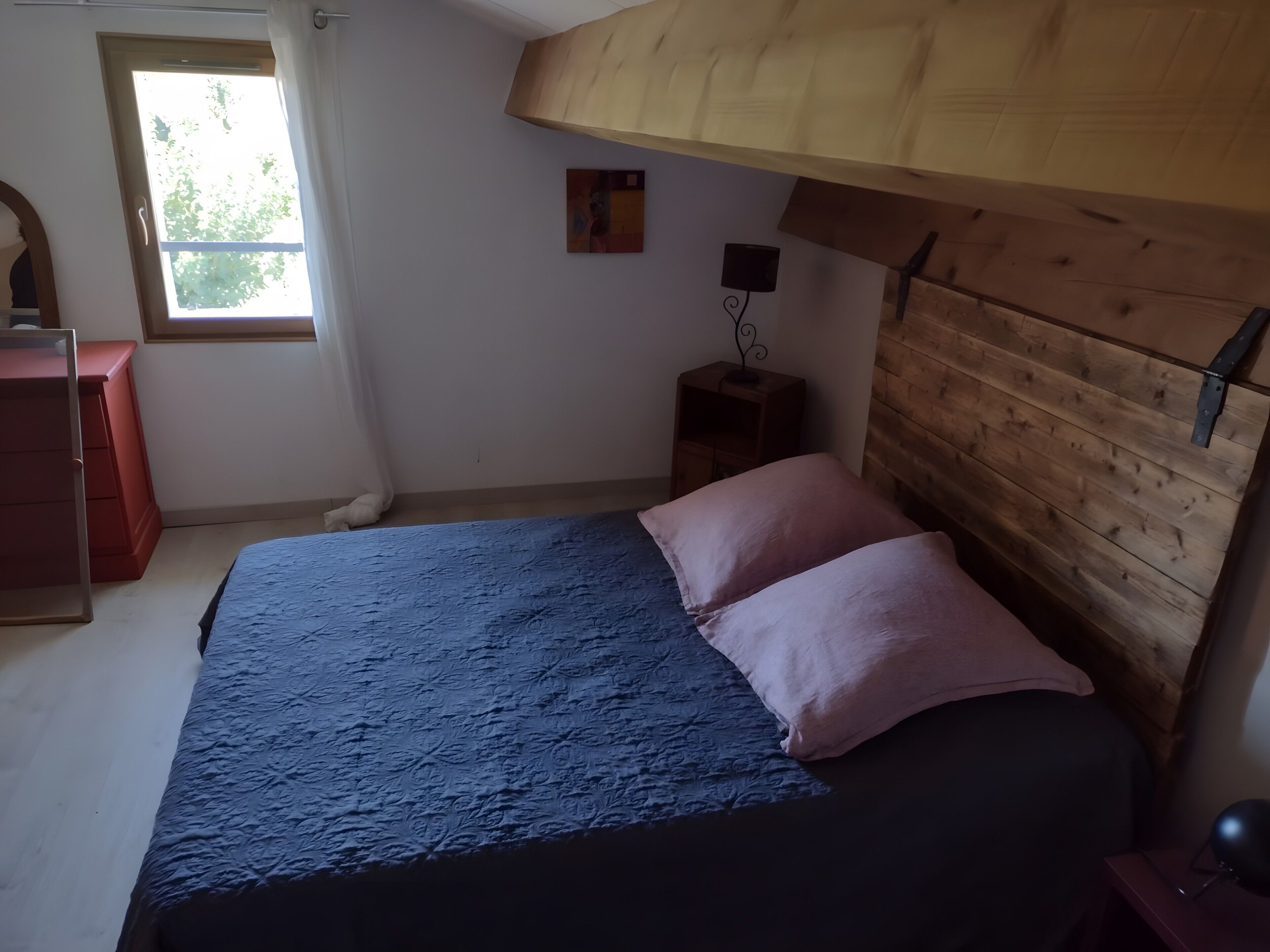 A bedroom with a bed, a wooden headboard, a nightstand, a dresser, and a window.