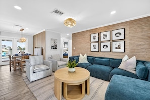 A modern living room with a blue sofa, striped armchairs, a round wooden coffee table, and framed pictures on the wall.