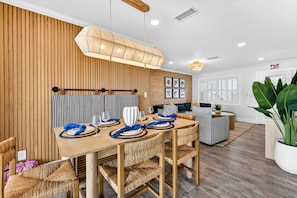 A dining area with a wooden table set for four, surrounded by wicker chairs, a striped wall, and a hanging light fixture.
