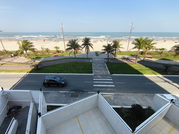 A view of a beach with palm trees, a road, and a parked car.