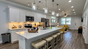 A modern kitchen with white cabinets, a large island with bar stools, stainless steel appliances, and pendant lighting. - 2 Luxe Chalets • Pool • Beach • Parking •Sleeps 12 (Bay St. Louis)